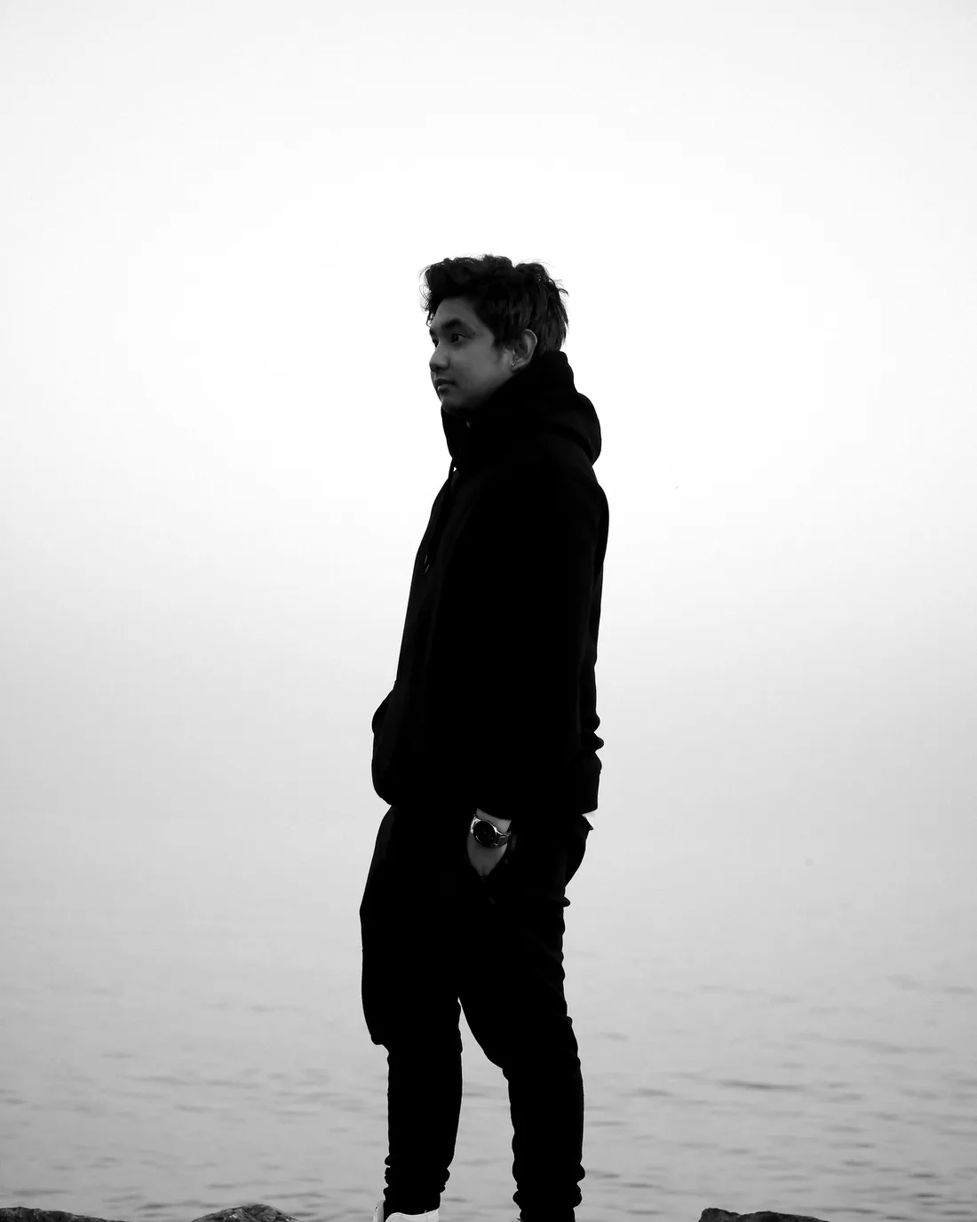 Joven con buzo negro frente al mar en blanco y negro