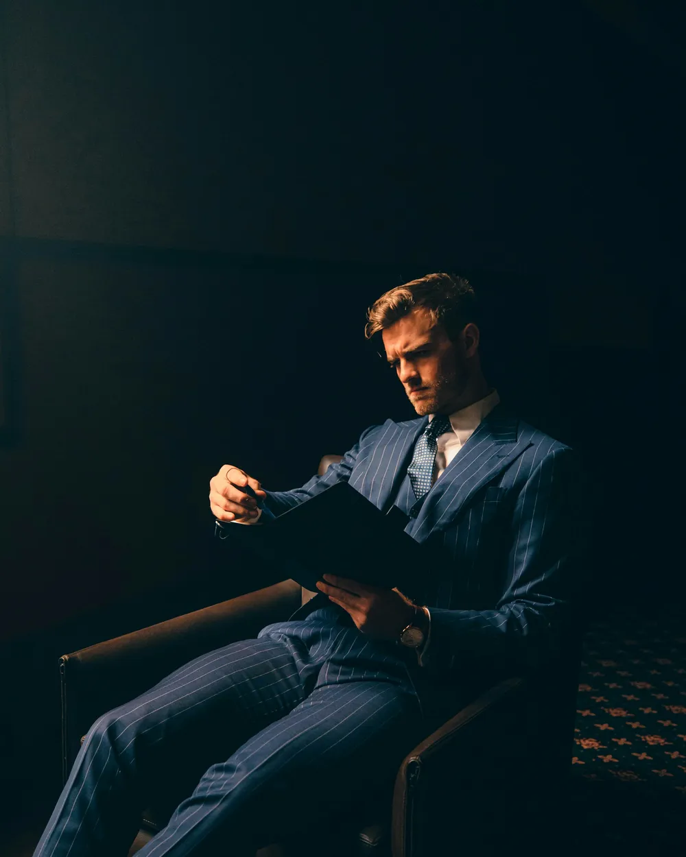 Hombre con traje azul sentado en penumbra